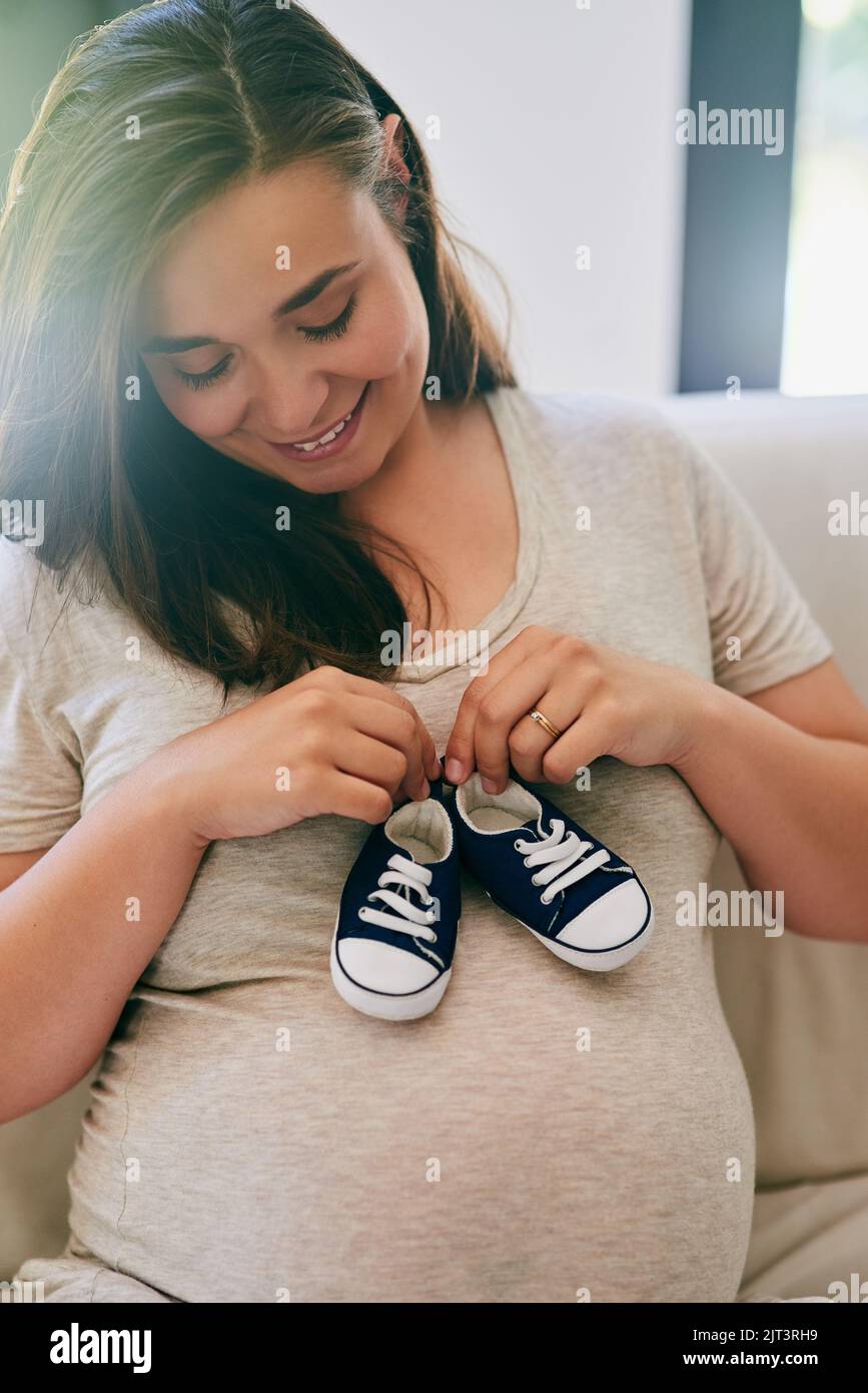 La donna incinta che tiene le scarpe del bambino contro il ventre. Foto Stock
