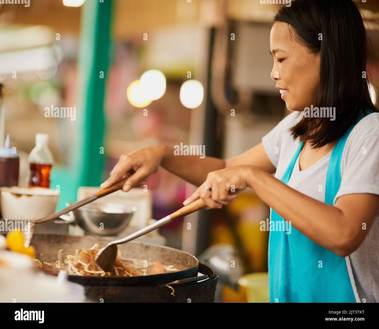 Un venditore di cibo felice che prepara un piatto tailandese in un mercato alimentare. Foto Stock