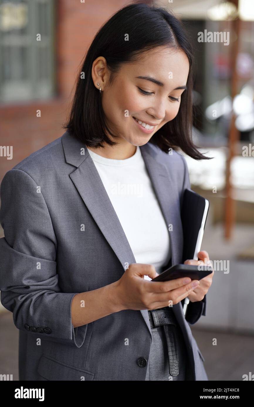 Giovane donna d'affari asiatica felice indossando il vestito con telefono, verticale. Foto Stock