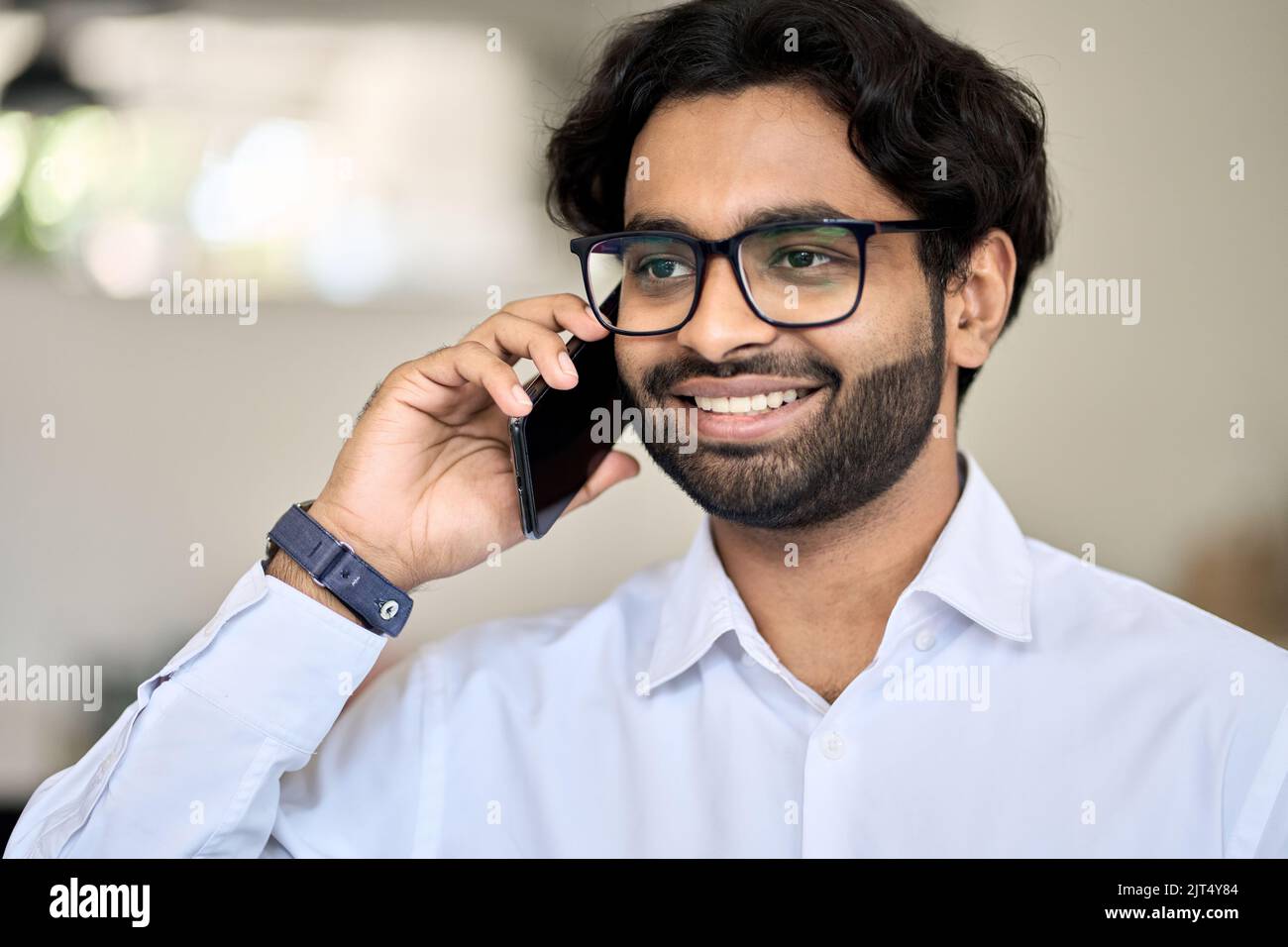 Giovane uomo d'affari indiano sorridente che parla al telefono facendo una chiamata. Foto Stock
