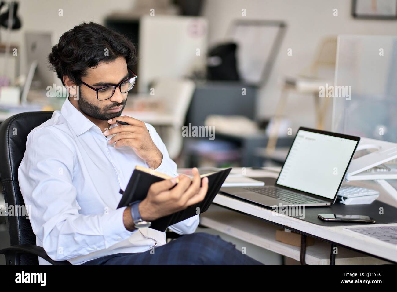 Occupato uomo d'affari indiano che pianifica il programma nel notebook che lavora in ufficio. Foto Stock