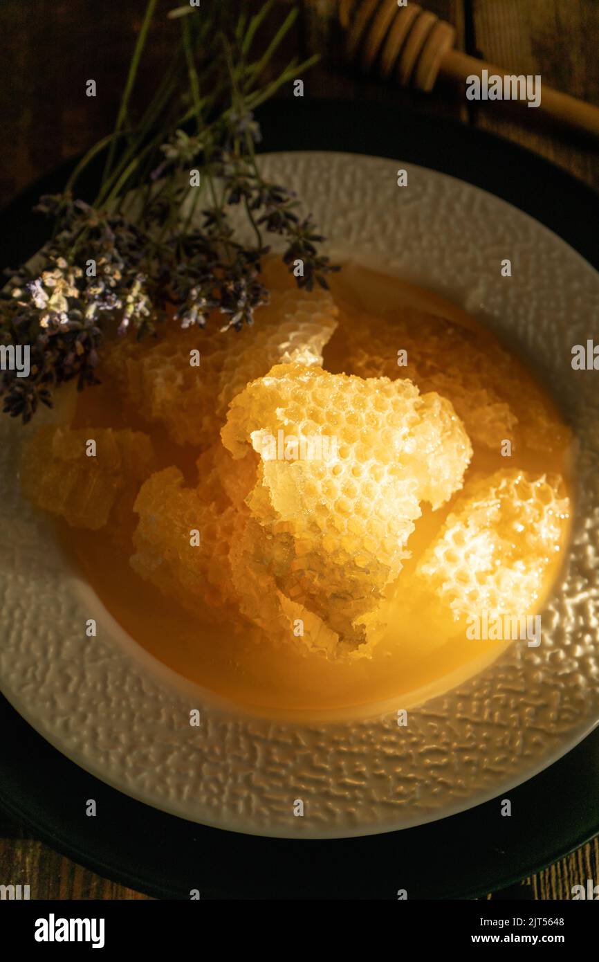 Miele e nido d'ape su un piatto bianco. Cibo dolce in una ciotola sul tavolo. Un prodotto dell'apicoltura. Fiore di lavanda. Foto Stock