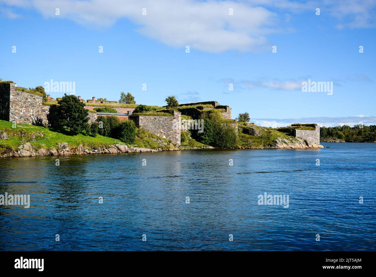 Un mare con fortificazioni ed edifici coperti da alberi lussureggianti a Suomenlinna, Helsinki, Finlandia Foto Stock
