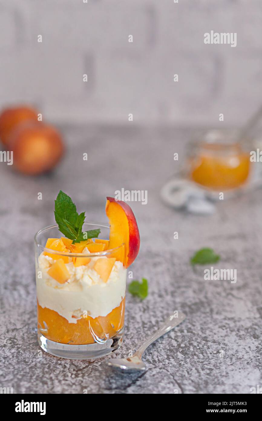 Dessert alla pesca in una tazza di vetro con crema cagliata e marmellata di pesche. Foto Stock