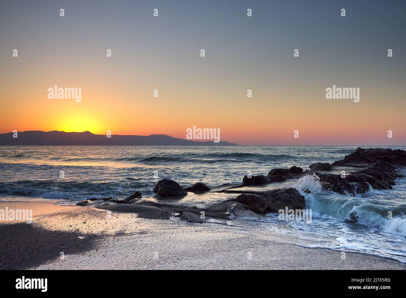 Il mare e le onde si schiantano contro un molo o un molo all'ora del tramonto Foto Stock