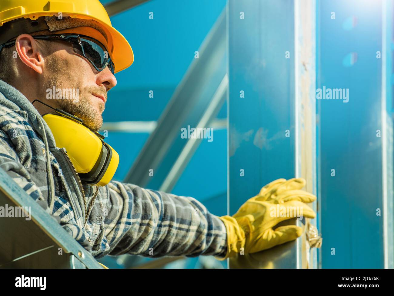 Lavoratori del settore edile caucasico che indossano un cappello giallo duro e occhiali da sole che soggiornano accanto al telaio dell'edificio in alluminio. Foto Stock