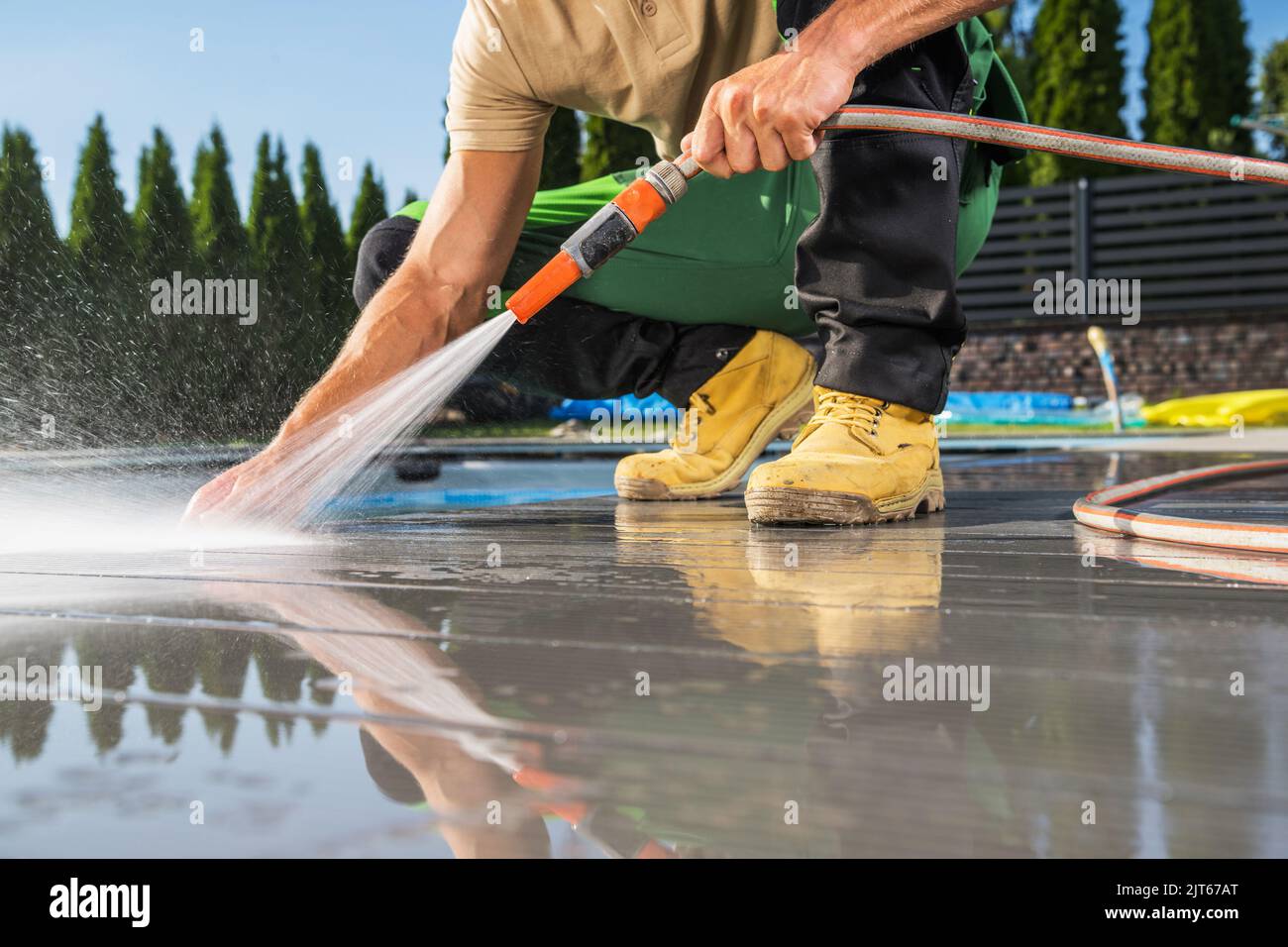 Gli uomini caucasici che lavano la sua piscina coperta composita fatta usando il tubo dell'acqua. Ordine di manutenzione del cortile. Foto Stock