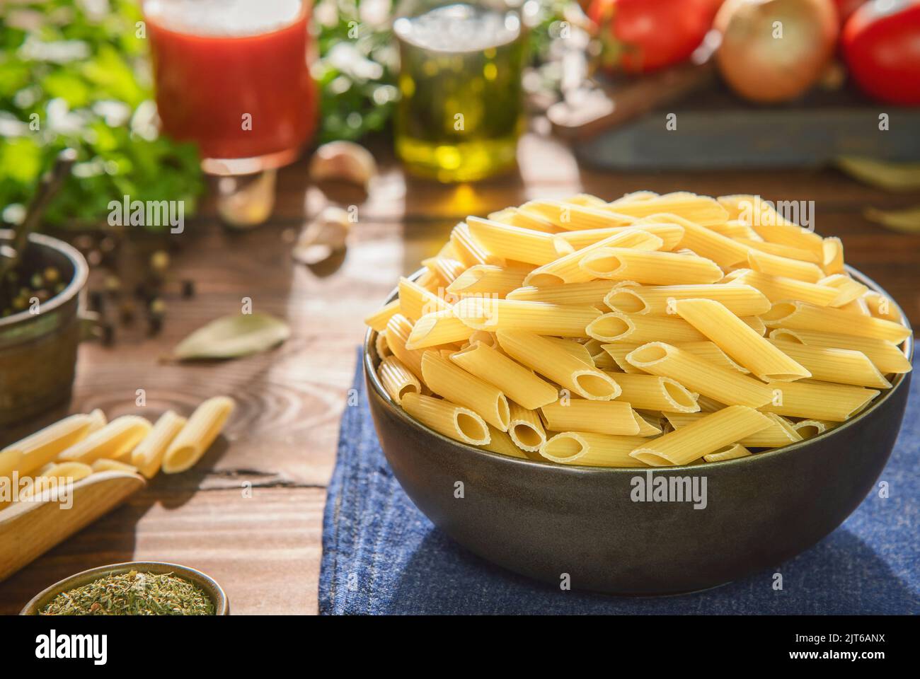 Recipiente per pasta di penne crude con ingredienti freschi su fondo rustico in legno. Foto Stock