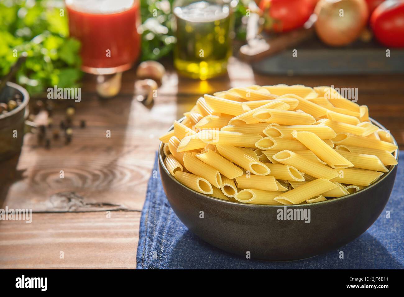 Recipiente per pasta di penne crude con ingredienti freschi su fondo rustico in legno. Foto Stock