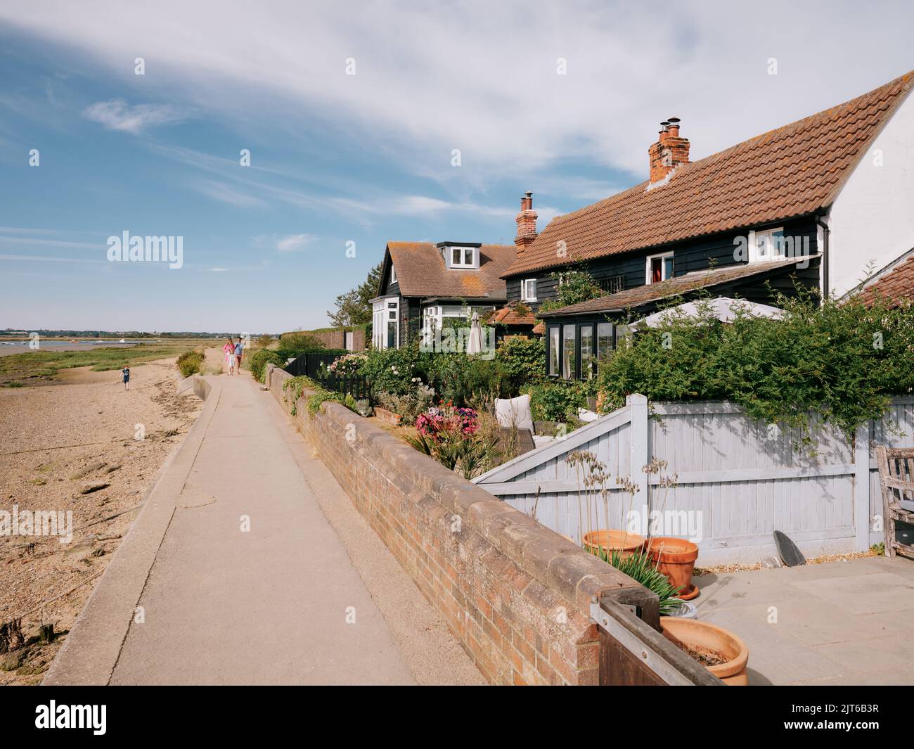 Camminando lungo il sentiero della costa estiva passò l'architettura del cottage sul lungomare e i giardini di West Mersea, Mersea Island, Essex, Inghilterra UK Foto Stock