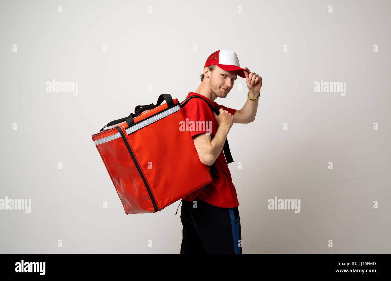 Vista laterale della consegna uomo in uniforme rossa portare zaino termico pieno di cibo, alimentari ai clienti. Servizio di consegna cibo. Foto Stock