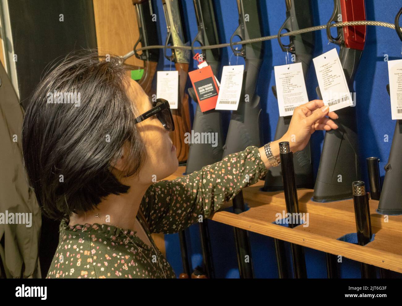 Una cliente asiatica guarda i fucili a 12 fori in vendita nel negozio del Southdown Gun Club & Shooting School, Findon, West Sussex, Regno Unito. Foto Stock
