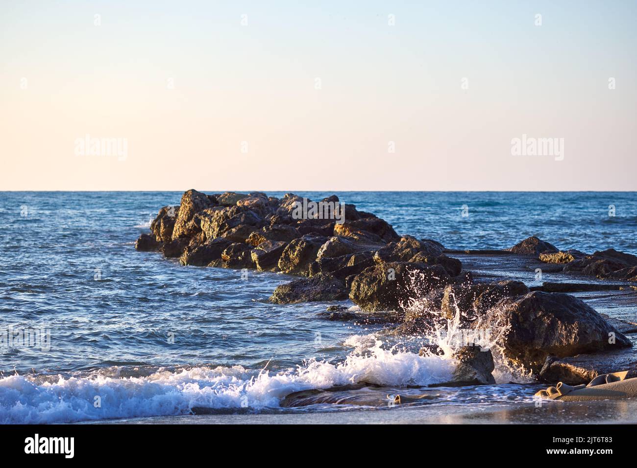 Il mare e le onde si schiantano contro un molo o un molo al tramonto a Chania Creta - Grecia Foto Stock