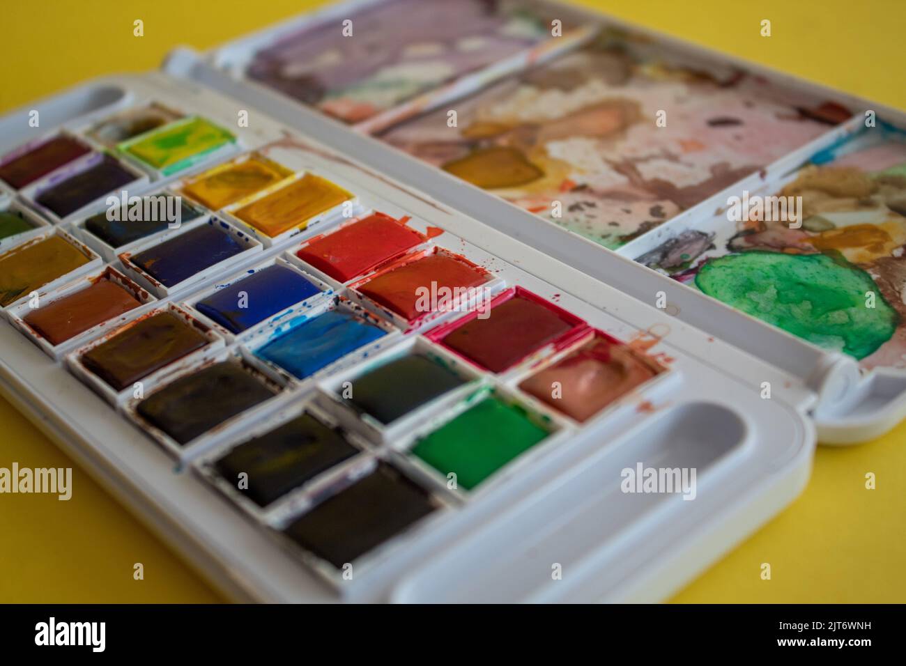 Tavolozza di acquerelli colorati e primo piano con pennello, sfondo giallo isolato, ritorno a scuola, messa a fuoco selettiva, effetto rumore Foto Stock