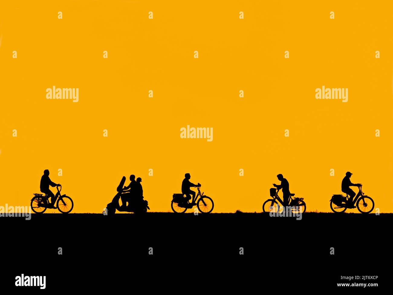 In estate, lo scooter passa accanto ai ciclisti e l'uomo in bicicletta per controllare il suo smartphone che si trova in una silhouette contro il cielo arancione del tramonto Foto Stock