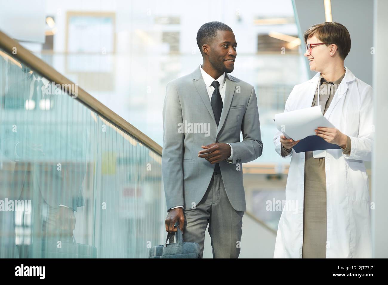 Ritratto di uomo d'affari nero sorridente che parla con una collega, mentre si cammina verso la macchina fotografica nella sala dell'edificio di uffici, spazio copia Foto Stock