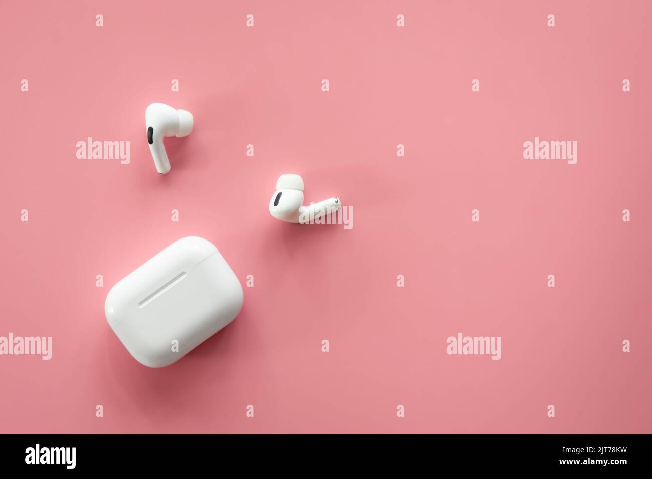 Cuffie intrauricolari wireless con custodia su sfondo rosa e disposizione piatta. Foto Stock