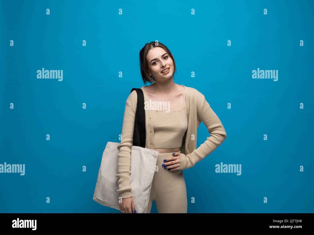 Bella donna brunetta in costume beige con sacco di cotone a spalla su sfondo blu. Concetto di mockup e zero sprechi. Foto Stock