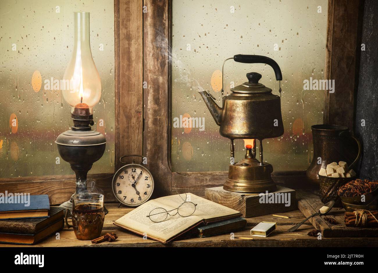 Vita morta classica con tè caldo posto con lampada d'epoca illuminata, vecchi libri, tazza di tè su tavolo rustico in legno. Foto Stock