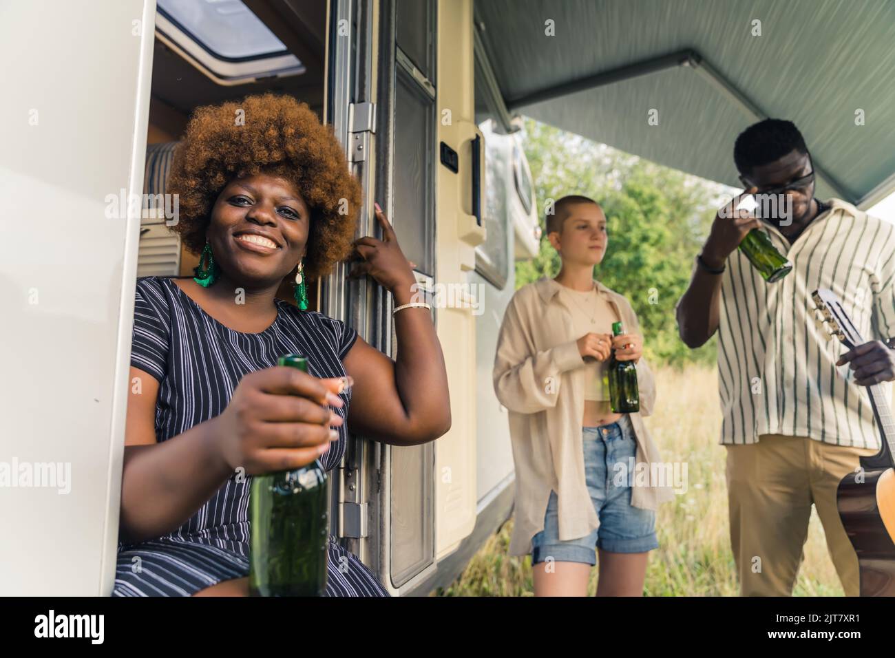 Allegra donna afro-americana seduta sul furgone e bevendo con i suoi amici. Foto di alta qualità Foto Stock