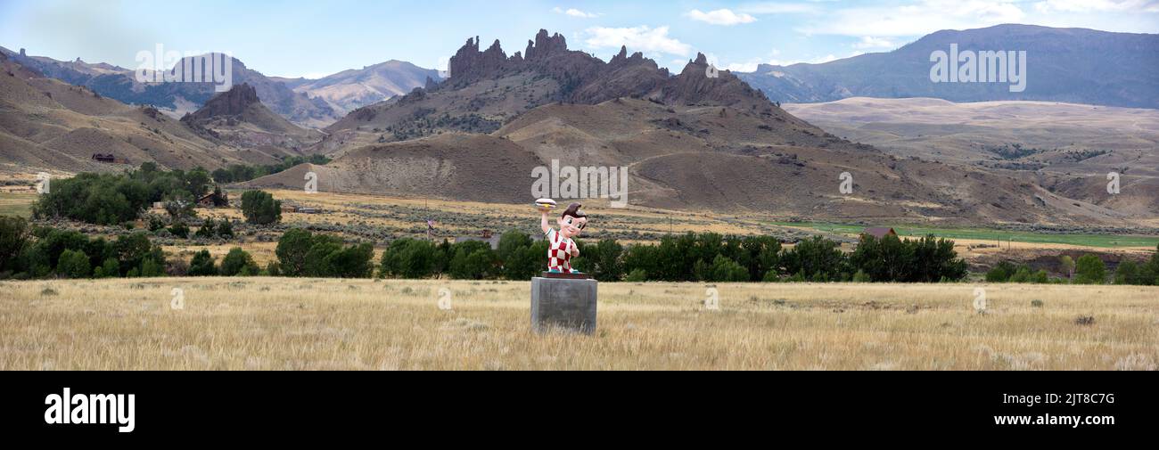 Panorama che mostra una statua retro del ristorante Big Boy del 1950s che tiene un hamburger sulle montagne Absaroka del Wyoming. Foto Stock