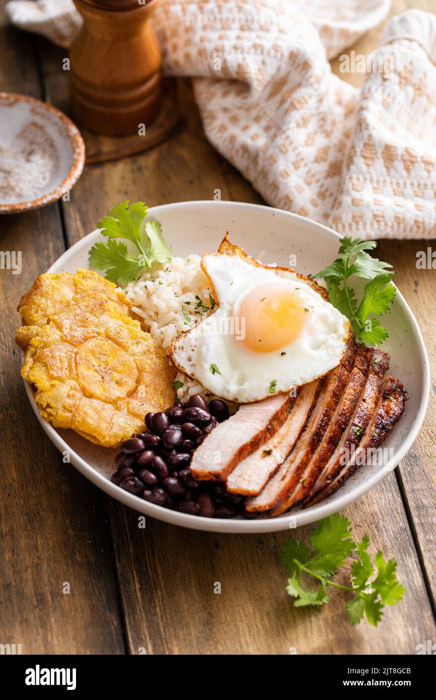 Colazione caraibica o latinoamericana con riso, fagioli, noccioli e maiale affettato condito con uova fritte Foto Stock