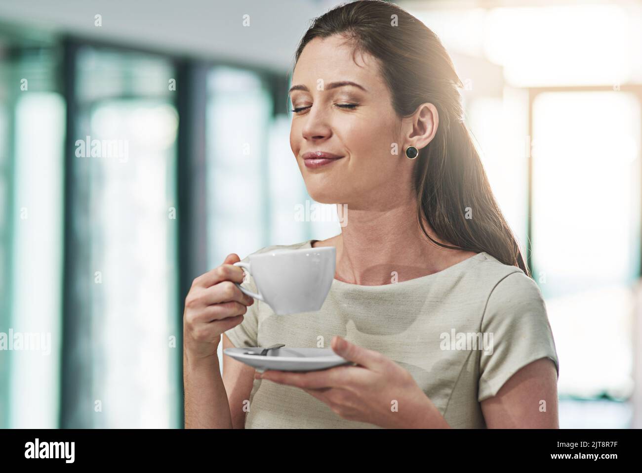 Niente di meglio di una buona coppa per migliorare il tuo umore. Una giovane donna d'affari che si diverte a gustare una tazza di caffè in ufficio. Foto Stock