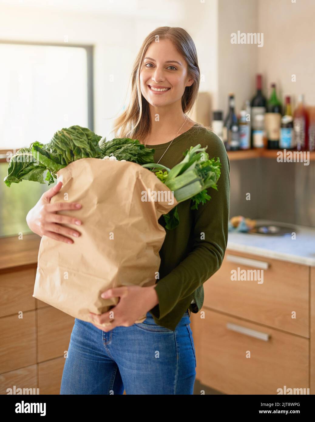 Fresco dal negozio alimentare. Ritratto di una giovane donna sorridente in piedi in cucina con un sacchetto di carta pieno di generi alimentari. Foto Stock