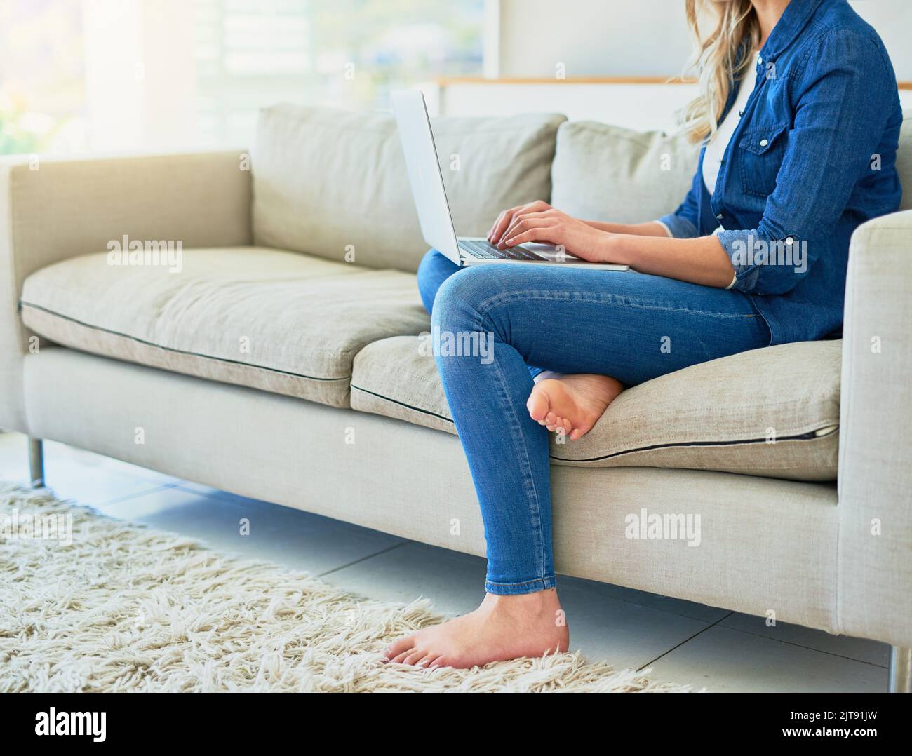 Comfort di casa. Una giovane donna irriconoscibile che usa il suo notebook mentre si siede sul divano di casa. Foto Stock