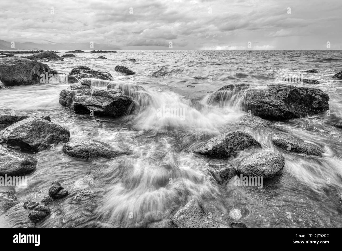 Un'onda dell'oceano sta rompendo su Una roccia di mare in un'immagine in bianco e nero ad alto contrasto Foto Stock