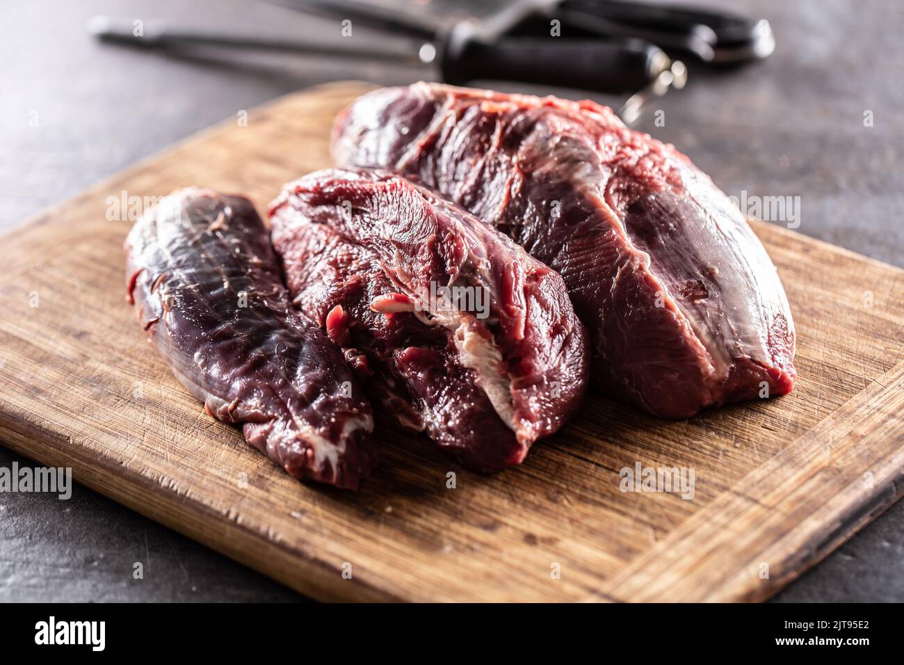 Grandi pezzi non tagliati di stinco di manzo crudo su un tagliere con coltelli sullo sfondo. Foto Stock