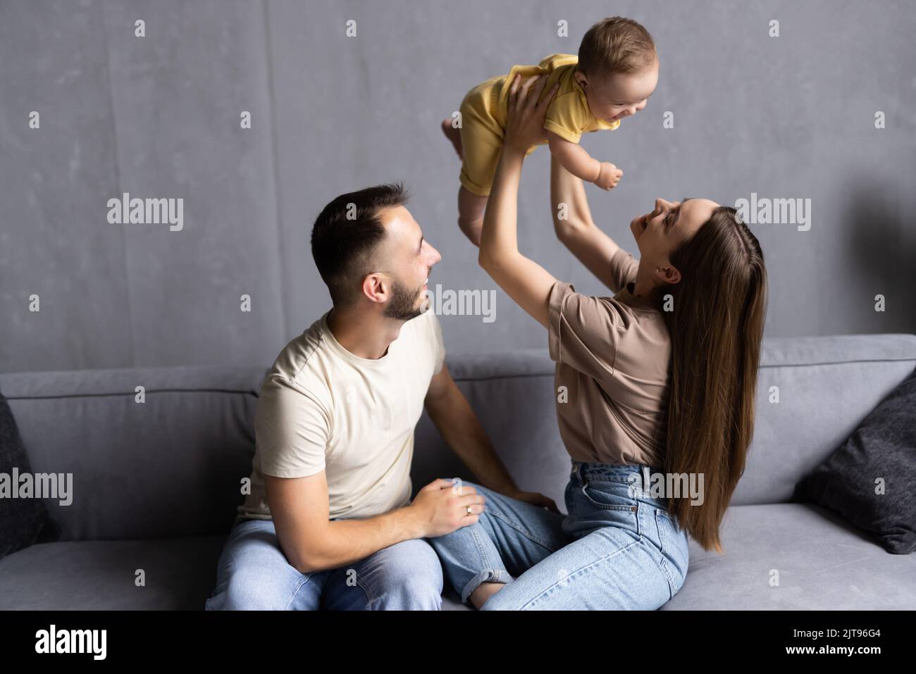 Felice giovane famiglia caucasica con piccolo figlio rilassarsi sul divano in soggiorno utilizzare moderno smartphone insieme. Foto Stock