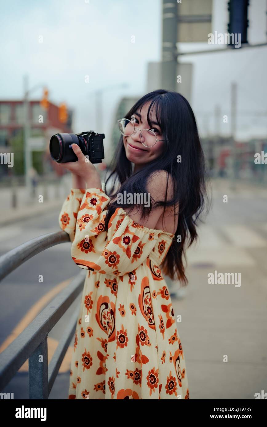 Un'immagine verticale di una donna asiatica che indossa un vestito che tiene la macchina fotografica e guarda la macchina fotografica in strada di Toronto Foto Stock