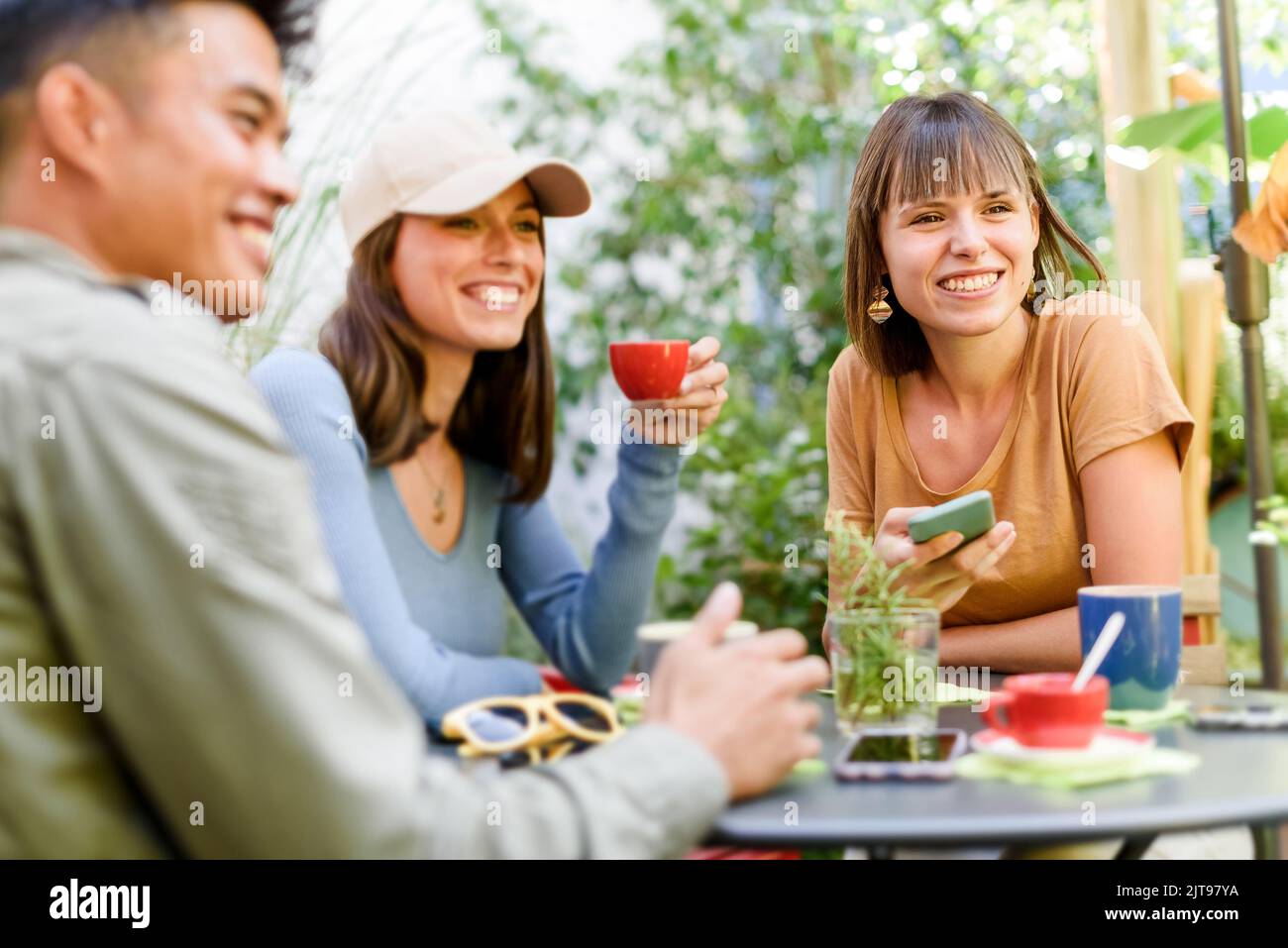 Amici spensierati seduti al tavolo con tazze di caffè e chiacchierando tra loro nel caffè all'aperto Foto Stock