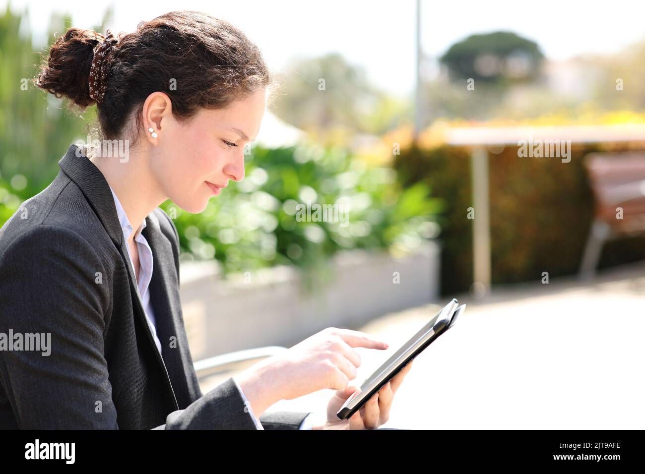Vista laterale ritratto di un dirigente seduto in un parco utilizzando un tablet Foto Stock
