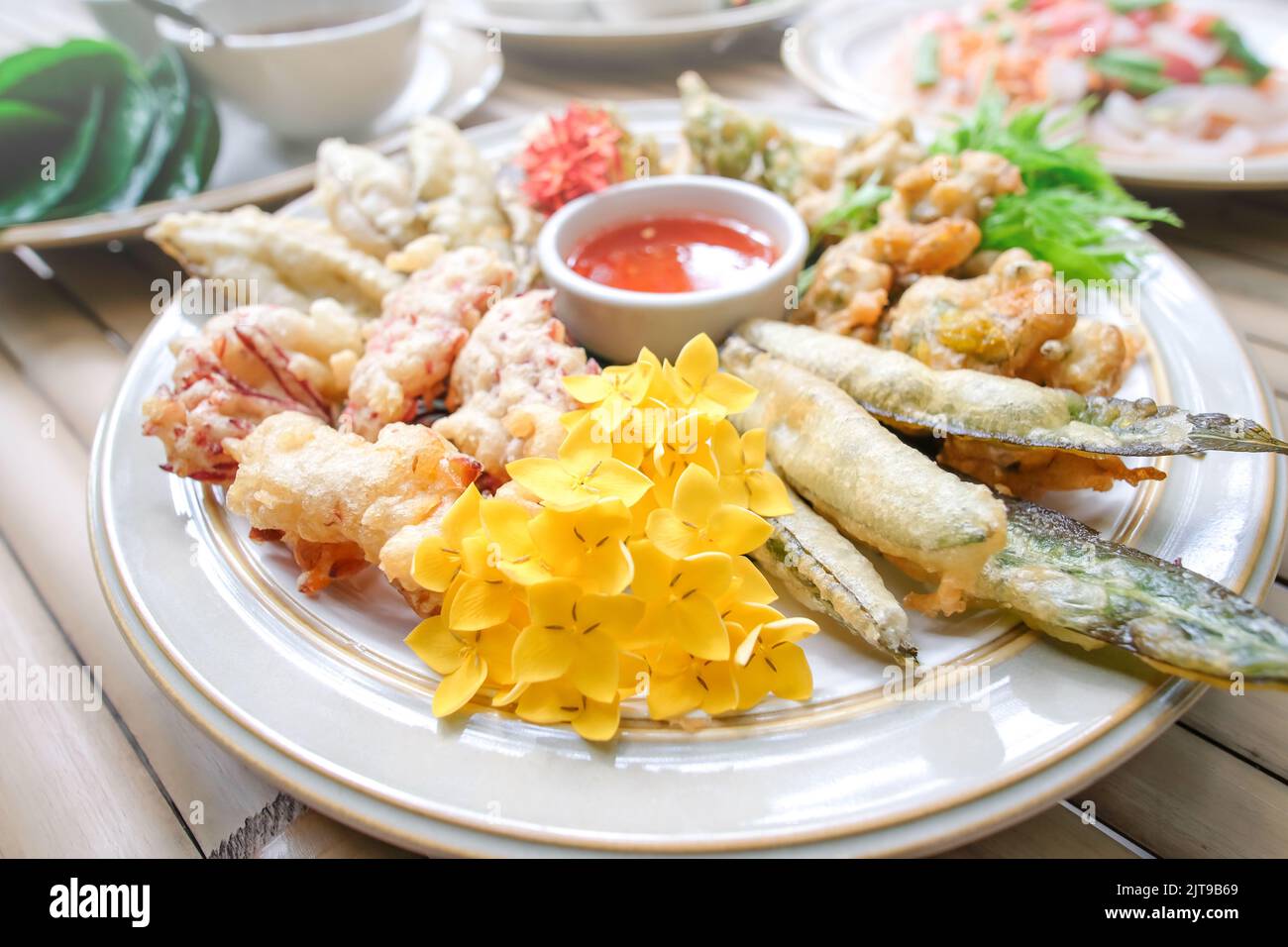 Fiori tropicali commestibili, foglie e verdure fritte servite su un piatto bianco poggiano sul tavolo di bambù. Cibo sano. Vista dall'alto. Primo piano. Foto Stock