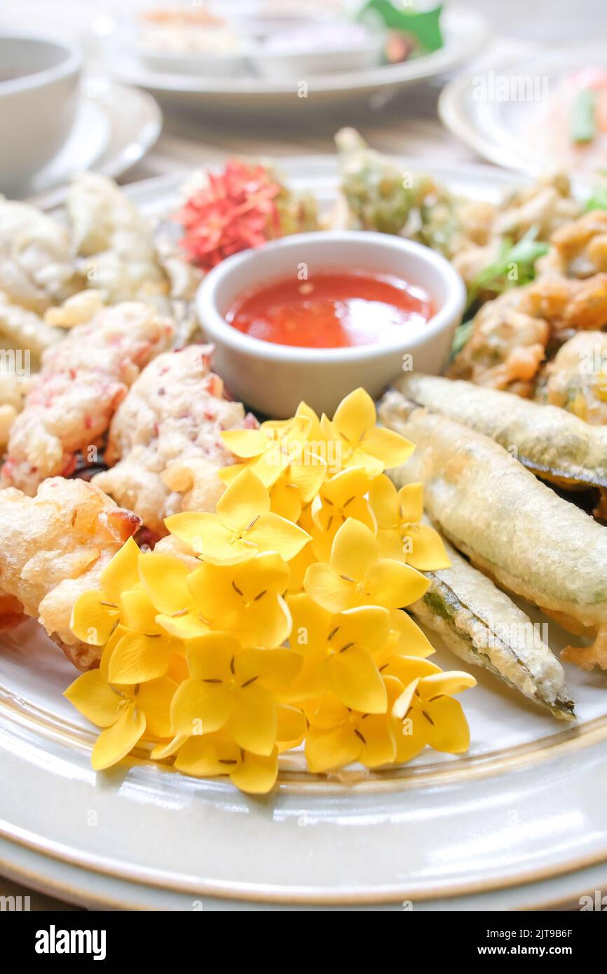 Fiori tropicali commestibili, foglie e verdure fritte servite su un piatto bianco poggiano sul tavolo di bambù. Cibo sano. Vista dall'alto. Primo piano. Foto Stock