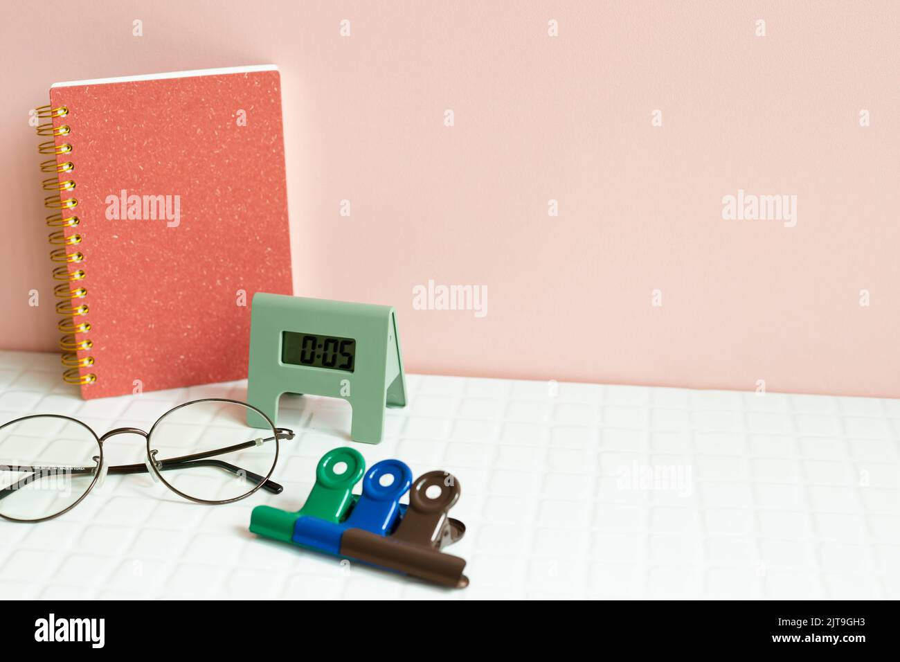 Tavolo da ufficio con notebook, occhiali, orologio, clip, forniture su scrivania bianca. Sfondo rosa parete Foto Stock