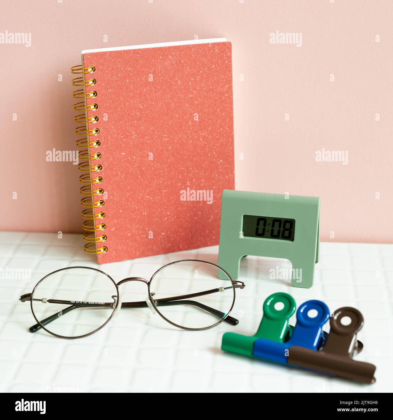 Tavolo da ufficio con notebook, occhiali, orologio, clip, forniture su scrivania bianca. Sfondo rosa parete Foto Stock
