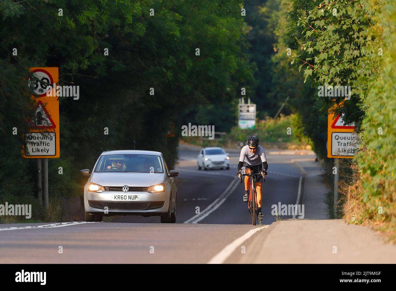 Un automobilista sorpassa un ciclista su Wakefield Road a Swillington, che ha due linee bianche che portano fino alla cima di una collina Foto Stock