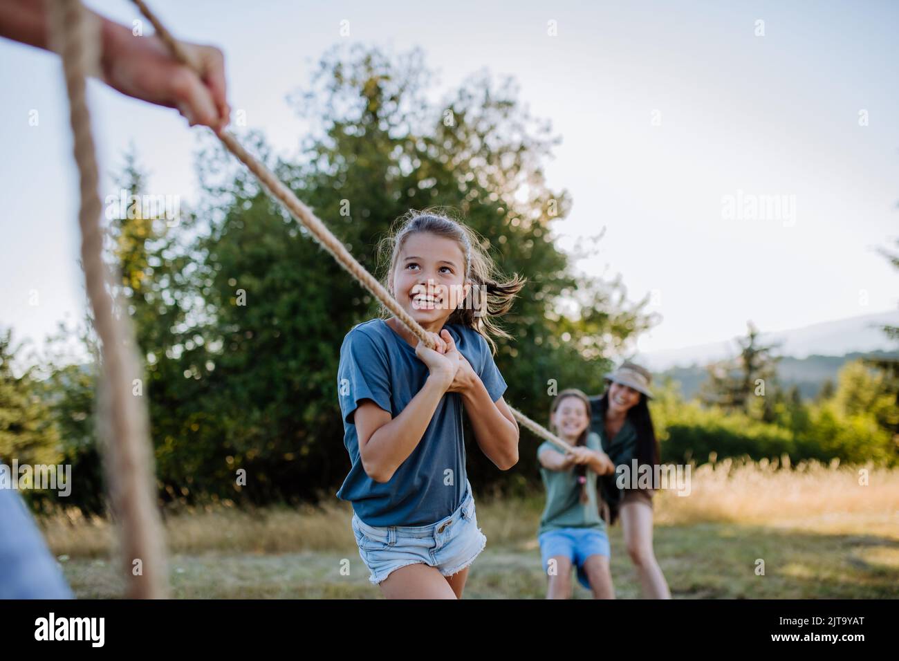 Famiglia giovane con i bambini felici che si divertono insieme all'aperto tirando la corda nella natura estiva. Foto Stock