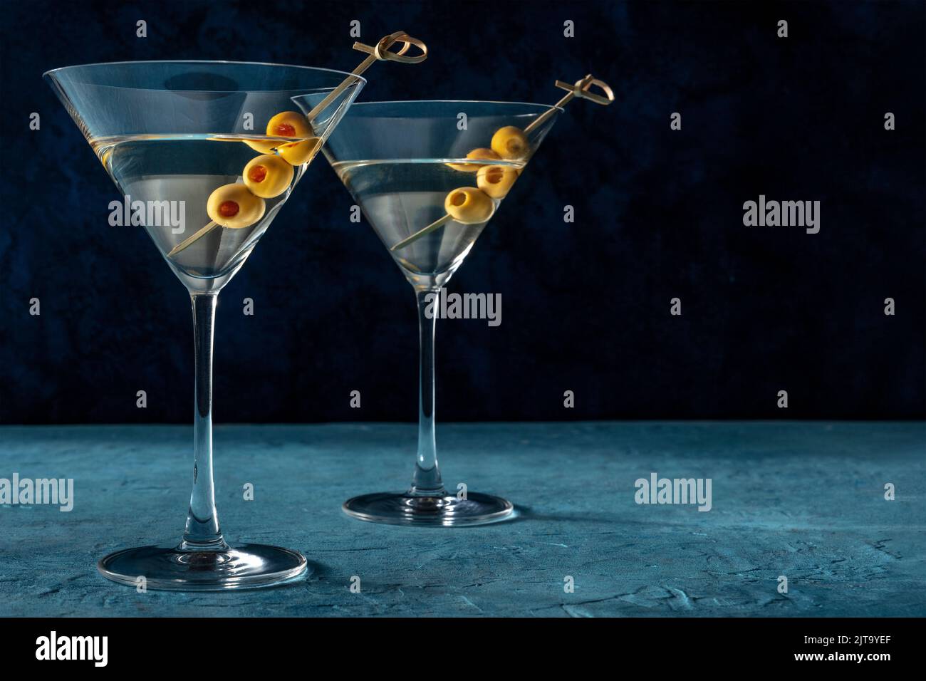 Martini, due bicchieri con olive speziate, su fondo blu scuro. Bevande alcoliche con un posto per il testo Foto Stock