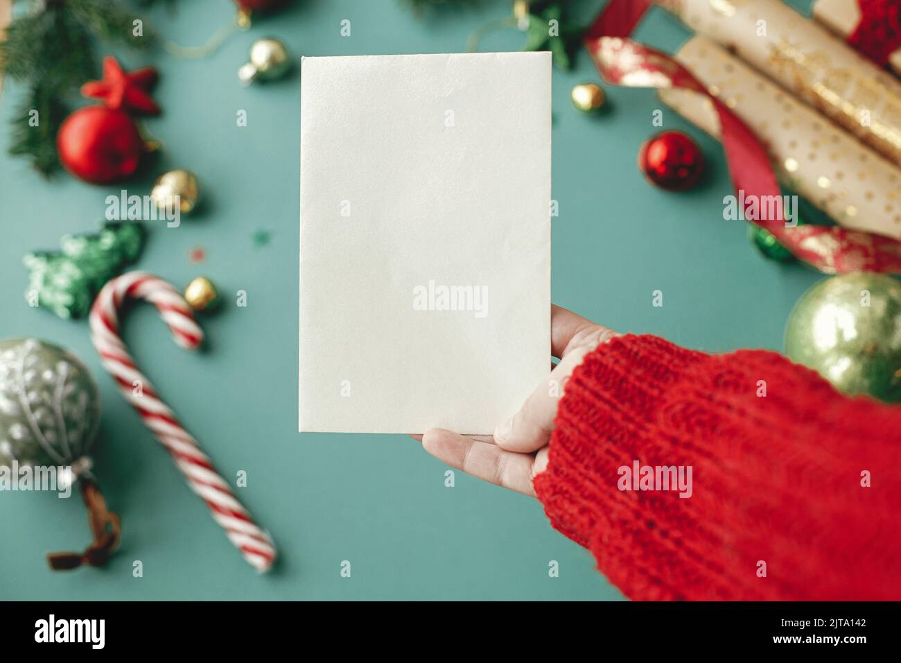 Mano che tiene la mock della scheda di natale in su. Biglietto d'auguri vuoto in mano donna sullo sfondo di eleganti decorazioni natalizie su sfondo verde. Cartolina Foto Stock