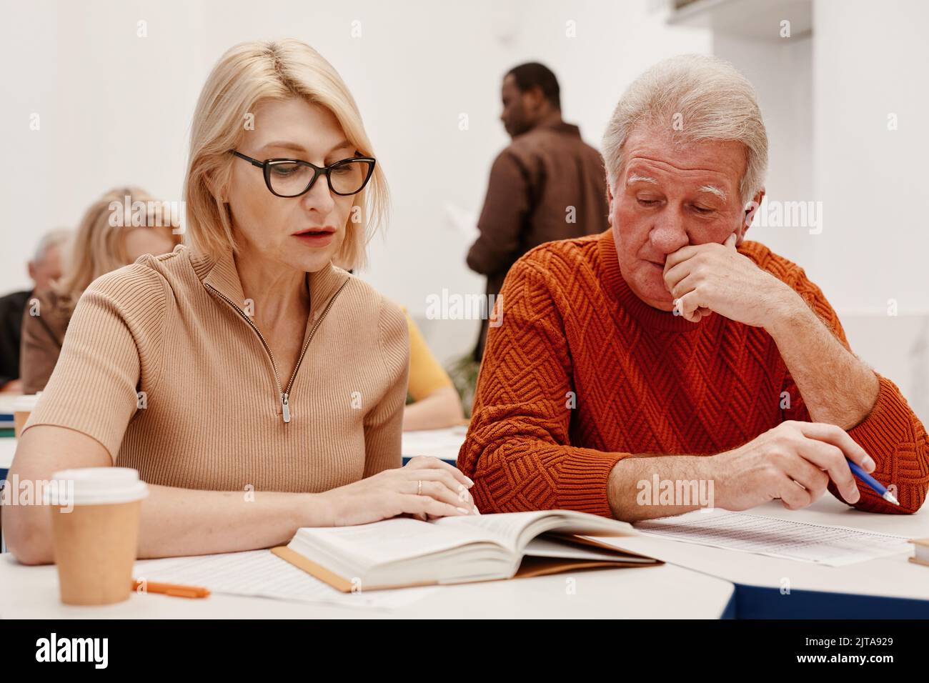 Coppia anziana seduta alla scrivania e lettura di un libro insieme durante la formazione in classe Foto Stock