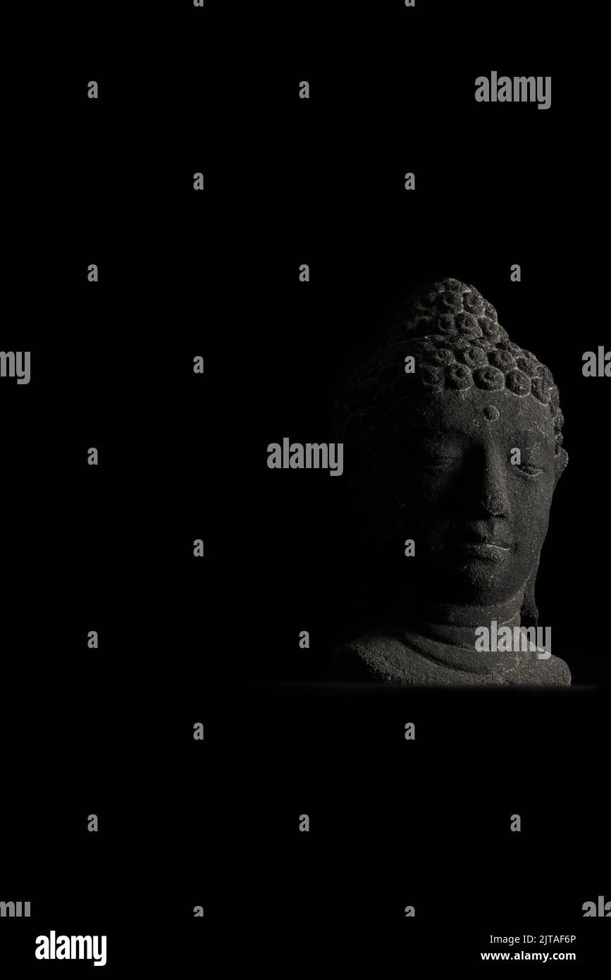 Statua della testa di Buddha in pietra con una suggestiva luce laterale Foto Stock