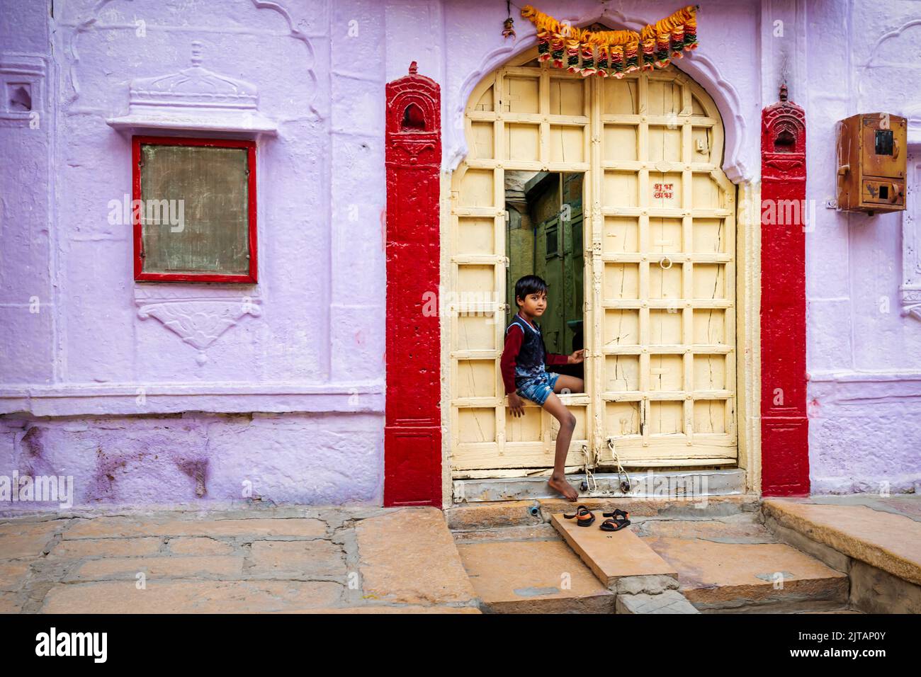 Un bambino che guarda fuori da una porta che si apre da un vecchio haveli, Jaisalmer, Rajasthan, India Foto Stock