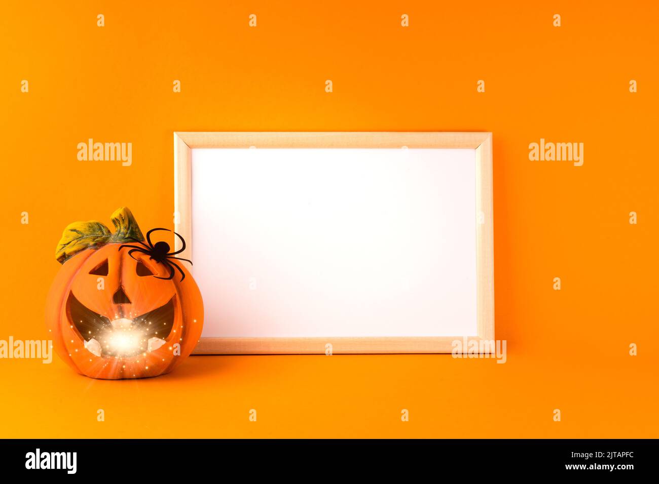 Concetto di festa di Halloween. Jack o lanterna con bokeh chiaro, decorazioni in carta fatte a mano, ragno e cornice bianca su sfondo arancione. Halloween Foto Stock