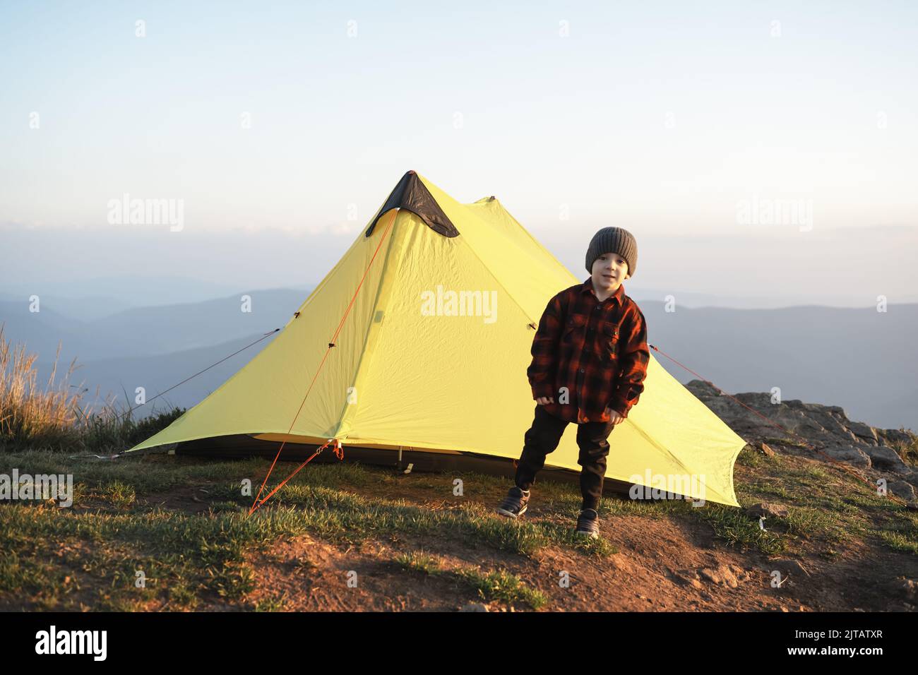 Piccolo bambino vicino a tenda gialla in montagne autunnali. Viaggia con bambino concetto Foto Stock