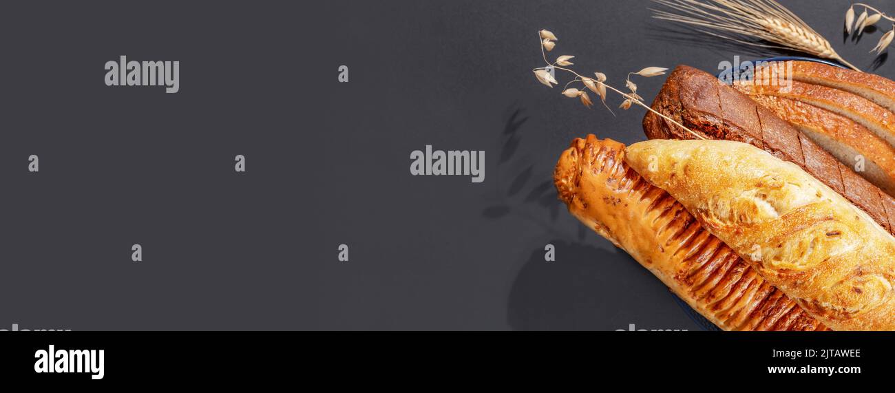 Banner alimentare con pane naturale fatto in casa. Pane fresco con spighe di segale e grano su fondo nero con spazio copia. Peste francese croccante Foto Stock
