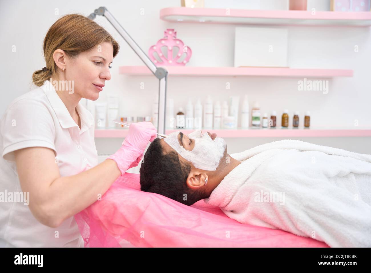 Cosmetician applicare la maschera di caolino alla pelle facciale dell'uomo Foto Stock